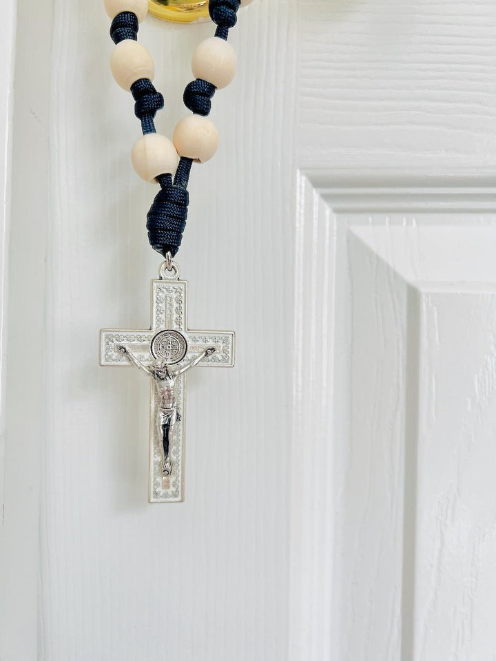 A door rosary with a silver-tone crucifix and St. Benedict Medal, featuring knotted beads in navy and gray colors, hanging on a door.