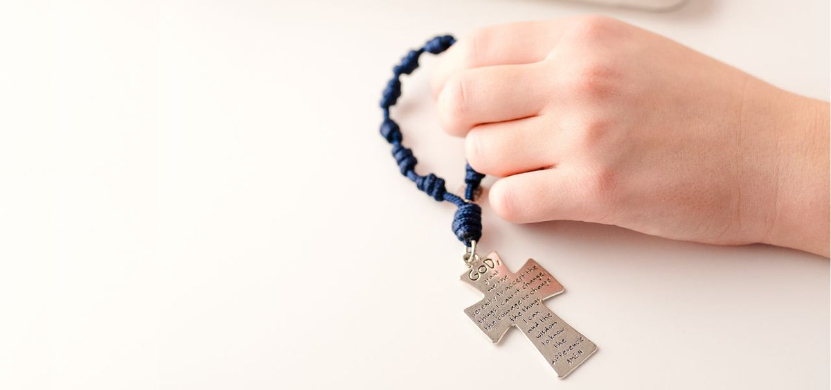 Hand holding a Serenity Prayer Pocket Rosary beside a computer.
