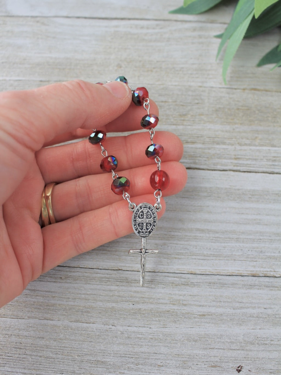 Hand holding a rosary with red multicolored beads on a wooden surface