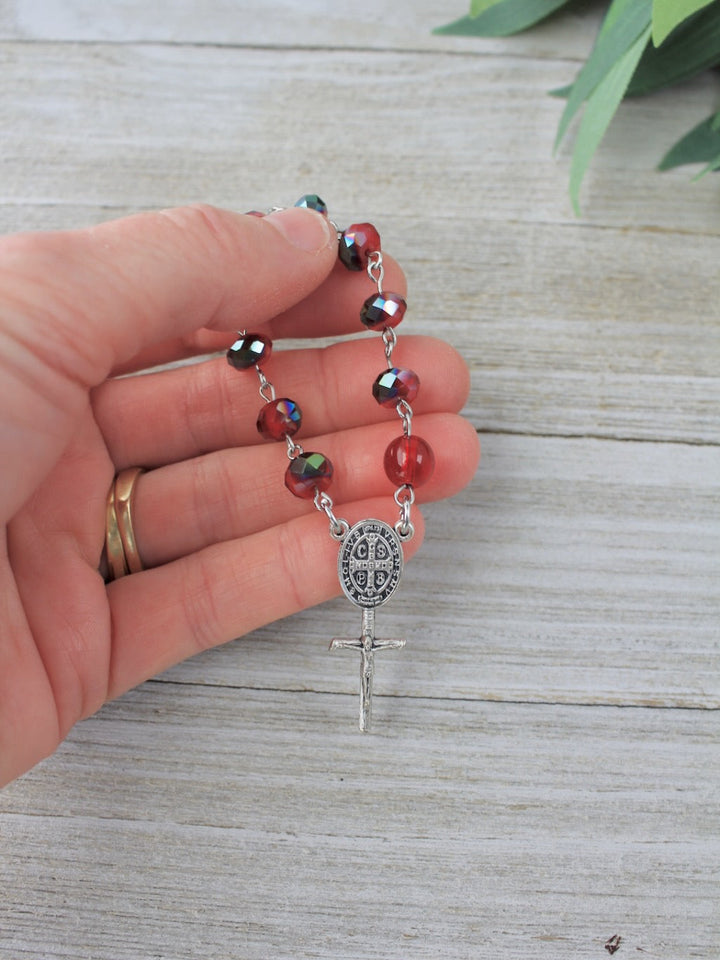 Hand holding a rosary with red multicolored beads on a wooden surface