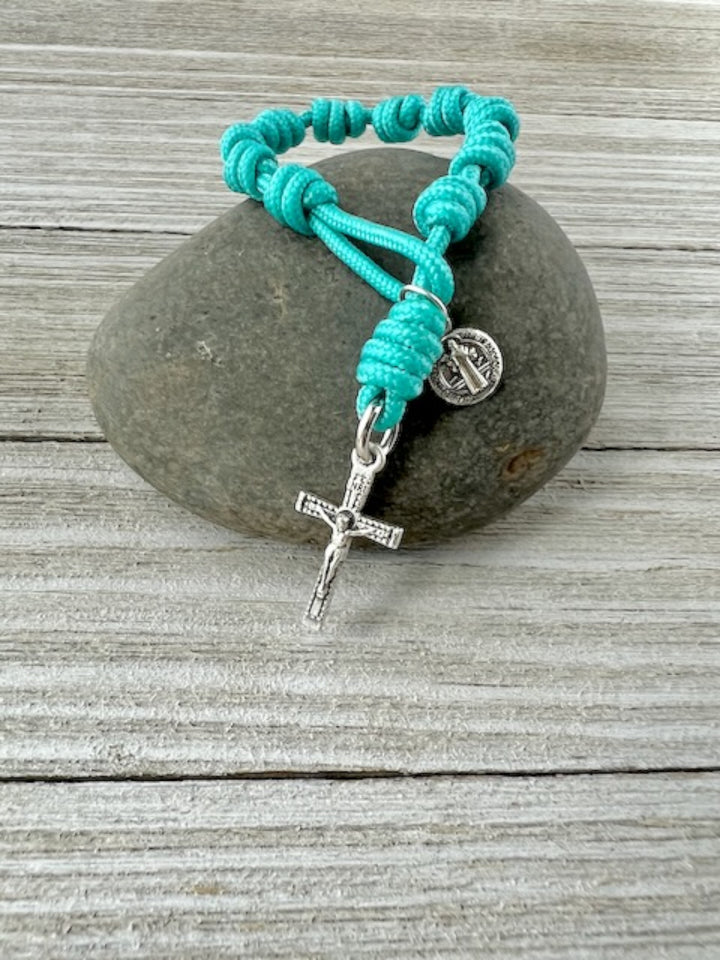 Turquoise one-decade Catholic pocket rosary with knotted cord, silver-tone cross and medal, handmade by Knots of Grace, displayed on rock