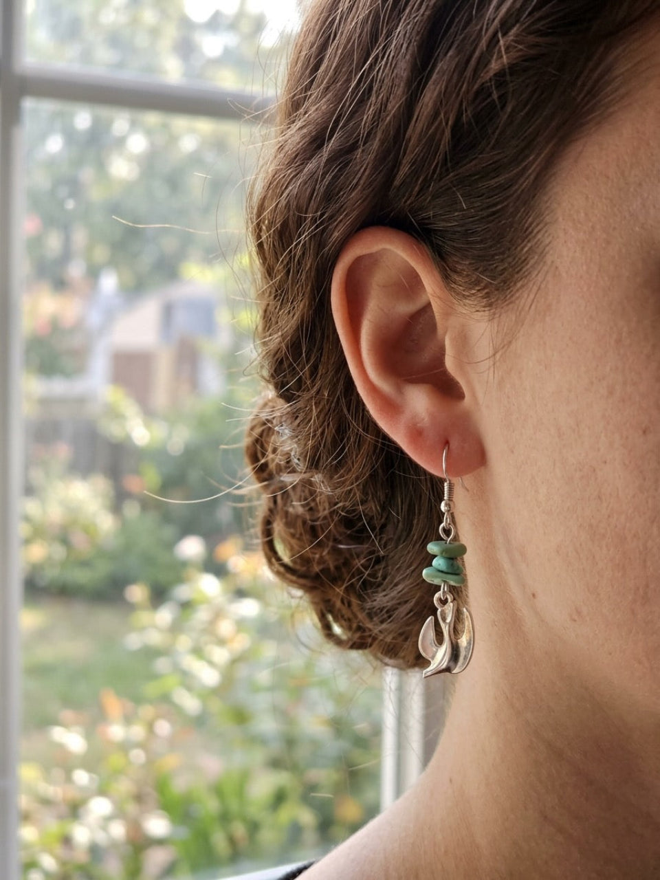 Side view of a woman with her hair styled in an updo wearing the handmade silver Holy Spirit dove dangle earring with stacked natural turquoise chips, demonstrating the scale, length, and fit of the jewelry.