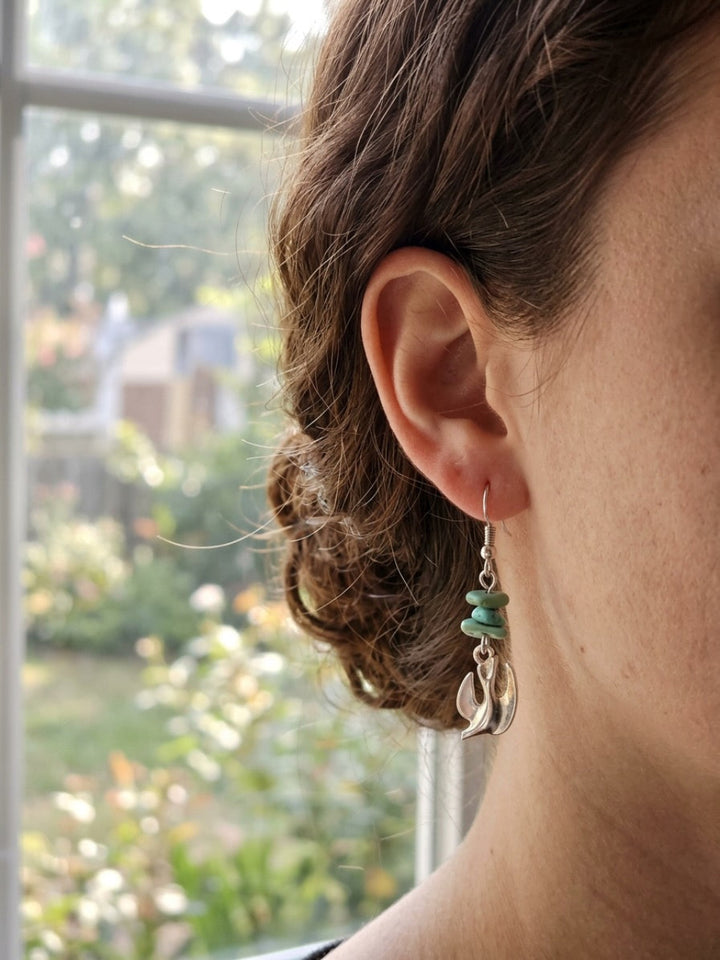 Side view of a woman with her hair styled in an updo wearing the handmade silver Holy Spirit dove dangle earring with stacked natural turquoise chips, demonstrating the scale, length, and fit of the jewelry.